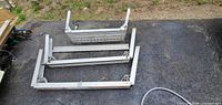 Three disassembled aluminum ladder support frames on ground