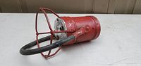 Side view of red beacon light showing cylindrical body, wire cage, and cable