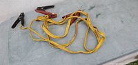 Full view of yellow jumper cables coiled on surface showing both clamp ends