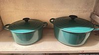 Both green enameled cast iron Dutch ovens side-by-side showing relative sizes, lids, handles and color.