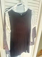 Front view of multiple tops on hangers highlighting black sleeveless tunic and taupe cardigan