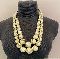 Full view of double-strand pale green bead necklace on display form