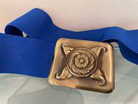 Front view of belt showing gold-tone buckle and blue elastic band