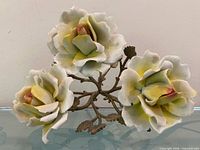 Front view showing three open porcelain roses, bud and brass stem