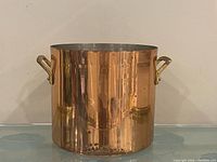 Front view of cylindrical copper pot with brass handles