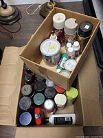 Two boxes filled with assorted spray paint cans, paint cans and craft paint bottles