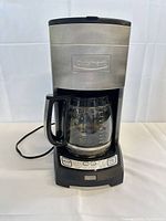 Full view of coffee maker showing stainless steel body, black base, carafe in place, power cord visible