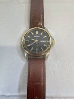 Front view of Seiko solar watch showing black dial, gold indices, brown leather strap