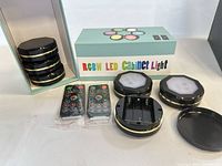 Six stacked black puck lights, two packaged remotes, three opened lights showing battery compartments, original box