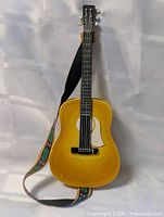 Full view of yellow plastic toy guitar with strap