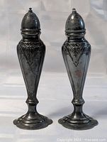 Front view of both ornate silver-plated shakers