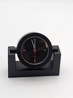 Front view of small black analog clock on rectangular base showing face and hands