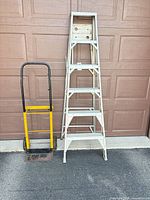 Ladder standing folded beside folded hand truck