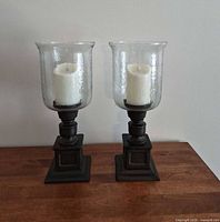 Pair of hurricane candle holders with flameless candles displayed on wooden surface