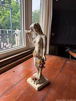 Front angled view of porcelain nude female figurine on square base with floral accents
