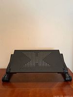 Front view of black laptop stand fully lowered showing perforated tray