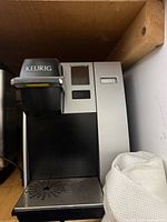 Front view of Keurig coffee maker showing silver front panel, black brew head, drip tray
