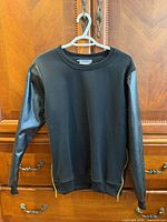 Front view of sweatshirt on hanger showing cotton body, faux leather sleeves, side zippers