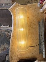 Sconce lit showing three bulbs and acrylic rod shade