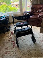 Front view of black Nexus rollator showing seat, backrest, storage pouch, wheels