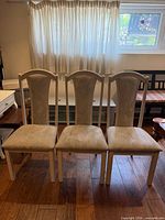 Front view of three matching beige/cream upholstered dining chairs