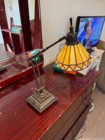 Full view of lamp on dresser showing stained glass shade lit, articulating arm, metal base