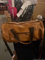Full view of tan leather duffel with strap and exterior pocket