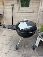 Front view of Weber black kettle grill with lid on, shovel and snow shovel nearby