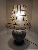 Full view of illuminated lamp showing base and capiz shell shade