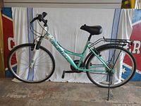 Full left side view of CCM teal/white 26-inch commuter bicycle with rack, fenders, kickstand visible