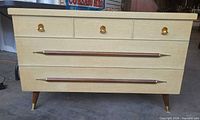 Front view showing cream finish, three brass pulls, two horizontal walnut handles, tapered legs with brass caps
