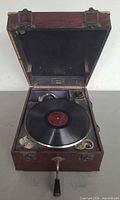 Phonograph open with record on platter, crank and sound box visible
