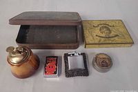 All six items: ceramic table lighter, two pocket lighters, State Express 555 tin, large metal box, round pill tin