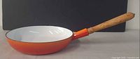 Side view of skillet showing orange exterior and wood handle