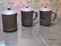 Front view showing all three mugs: one with calligraphy, two with bamboo leaf design, lids on