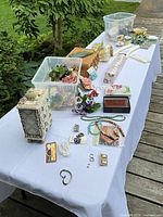 Overall lot displayed on table showing jewelry pieces, storage bins and chest
