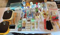 Overview of entire lot on table showing toiletries, toothbrushes, soaps, razors, combs, sink basins, wire dish rack, boxed dish rack, lids