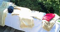 Mixed bedding items on outdoor table: quilts, throws, pillows, sheet sets