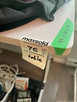 corner of white tabletop showing green tape with written dimensions