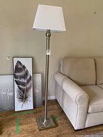 Full view of floor lamp beside sofa showing base, pole and shade