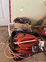 Overall lot showing bins of extension cords, box of bungee cords, and ropes leaning against wall