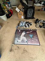 Lot overview showing both pairs of skates, trekking poles, baseball bat, and framed baseball print