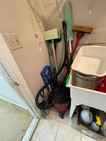 Overall view showing Shop-Vac, hose, assorted mops and squeegee beside laundry sink