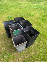 Front view of six black square planters on grass