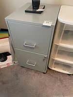 Front view of gray two-drawer filing cabinet beside plastic drawer unit