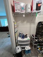 Shelf with two boxed Honeywell humidifiers, cylindrical humidifier, drawer organizer, steam iron, ironing board, additional humidifier at floor