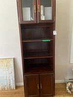 Full front view of tall wooden bookshelf showing upper glass doors, shelves, lower doors