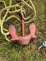 Red iron anchor marked 14 LB with attached rope resting on grass