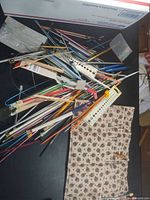 Pile of mixed knitting needles, plastic gauge, rulers, needle holder visible