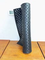 Rolled black perforated rubber mat standing vertically on wood surface